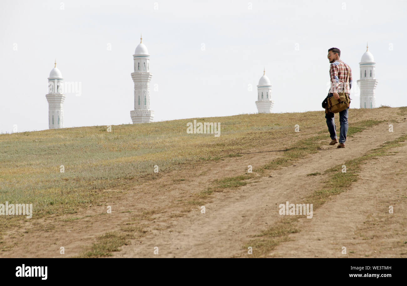Man walking towards the Hazrat Sultan Mosque in Nur-Sultan, Kazakhstan, while only the four minarets can be seen behind a hill. Stock Photo
