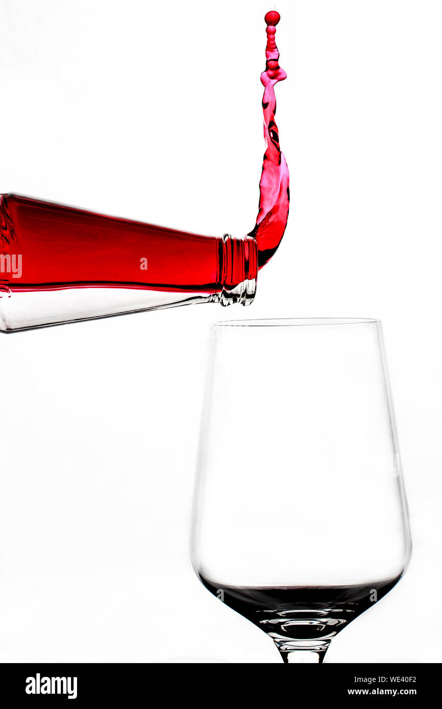 Upside Down Image Of Red Wine Spilling From Bottle With Glass Against
