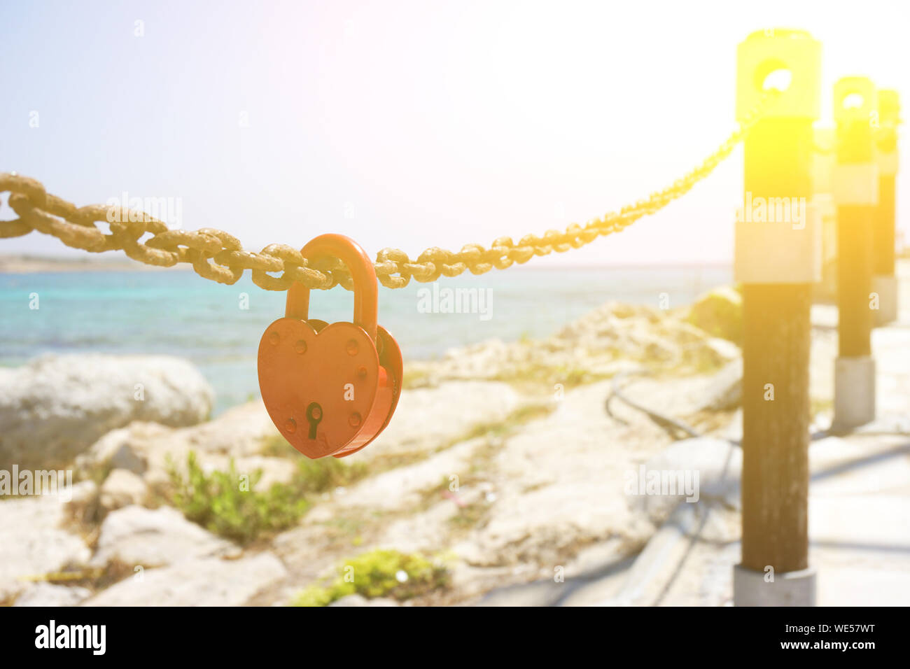 Red love padlock attached to chain. Rusty lock with heart shape carved hanging outdoors. Valentines day, unity, memory concepts. Stock Photo