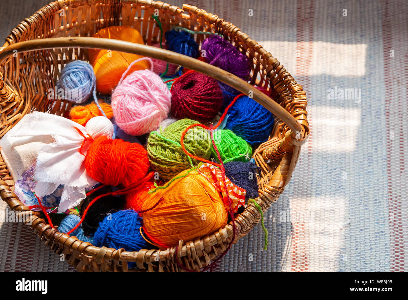 Multicolored yarn balls in a straw basket on a wooden table Stock