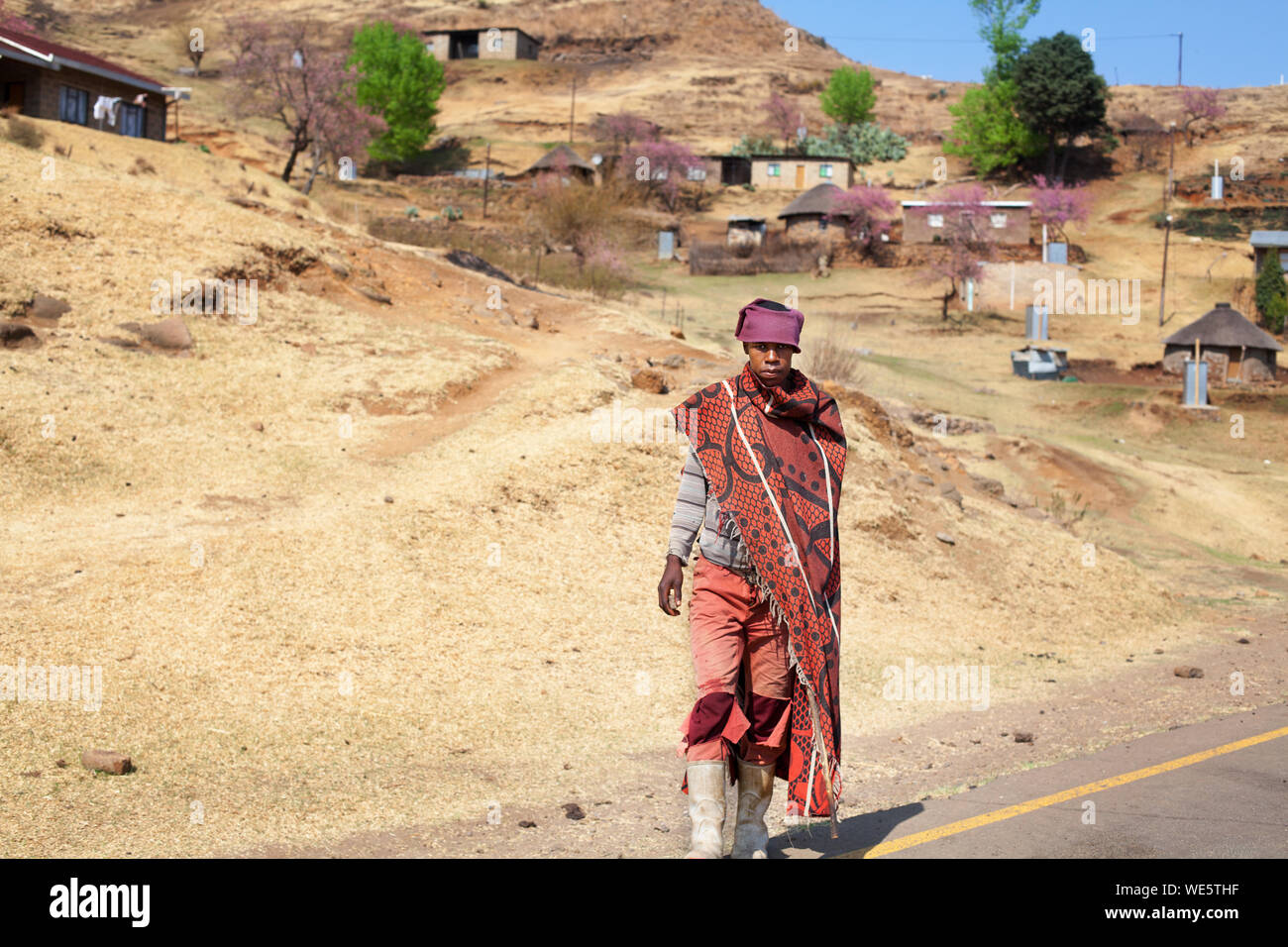 Semonkong, Lesotho - September 20, 2017: young african shepherd man in national red wool blanket dress and balaclava on rural high mountain road Stock Photo