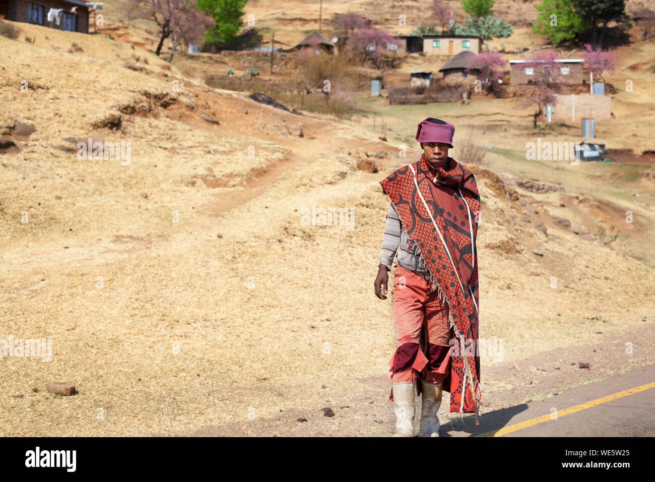 Semonkong, Lesotho - September 20, 2017: young african shepherd man in national red wool blanket dress and balaclava on rural high mountain road Stock Photo