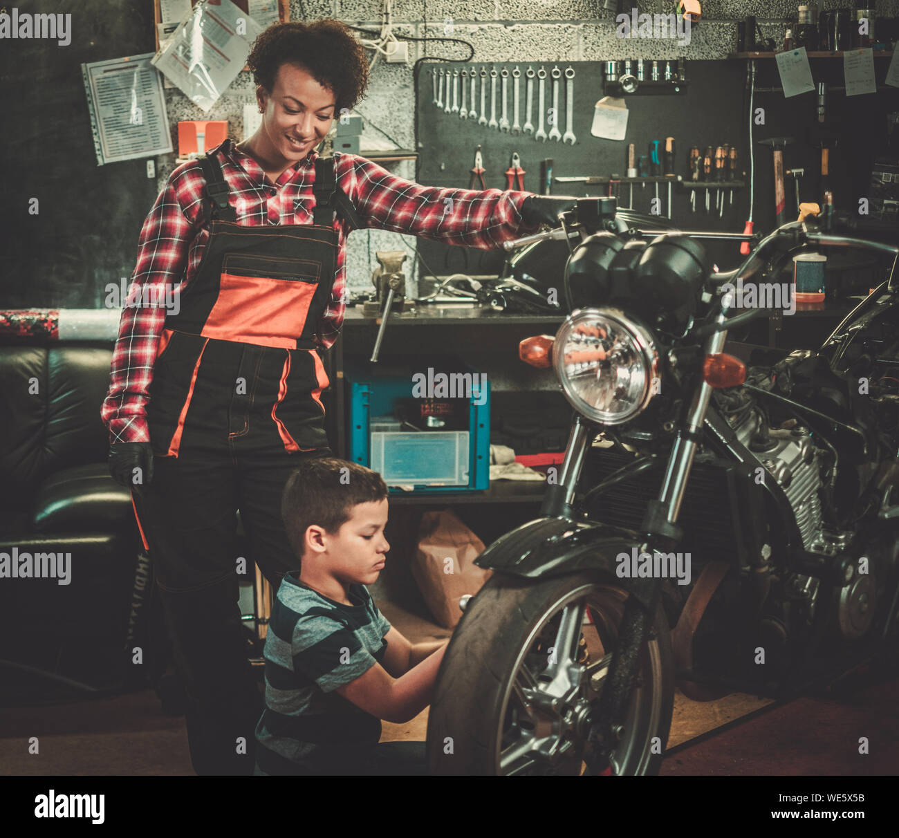 African american woman mechanic and boy helper repairing a motorcycle in a workshop Stock Photo