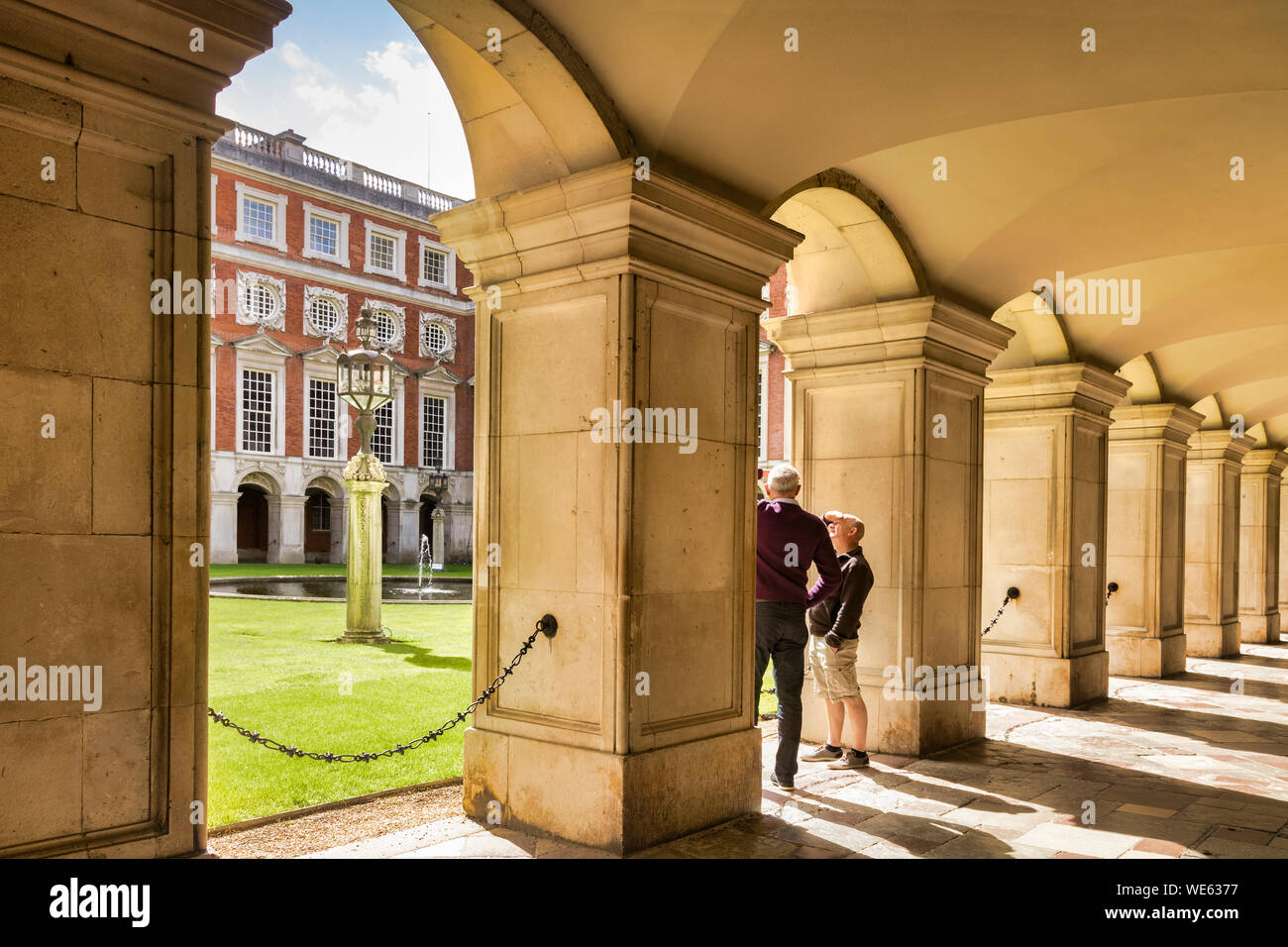 9 June 2016: Hampton Court, Richmond, London, UK - The Colonnade in Fountain Court, two male tourists sightseeing. The Palace was begun building in 15 Stock Photo