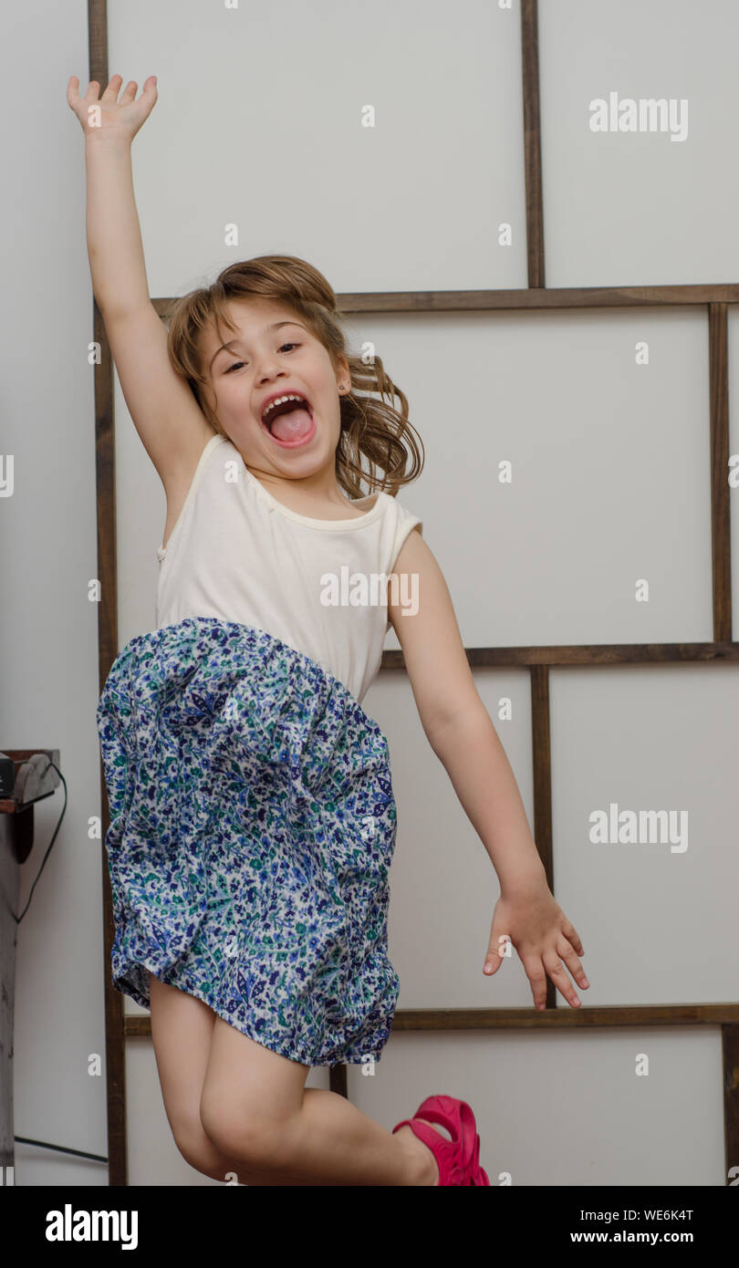 Portrait Of Excited Girl Jumping Against Wall At Home Stock Photo