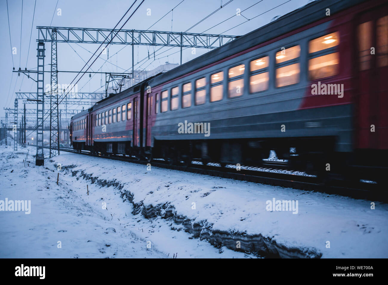 Train passing at speed in the snow. Lights are on inside the carriage. Passengers making their way home from work on a commuter train in the evening. Stock Photo