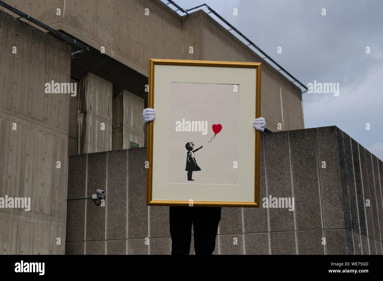 London, UK. 30th Aug, 2019. A Christie's employee poses with artworks 'Girl with balloon' by anonymous street artist Banksy at the Southbank Centre in London Friday, August 30, 2019. The Southbank Centre was near one of the original locations the artwork appeared in London. The screen prints will be on sale during an online only auction titled 'Banksy : I can't believe you morons buy this sh*t' presented by Christie's auction house between 11-24 September 2019. Photograph Credit: Luke MacGregor/Alamy Live News Stock Photo