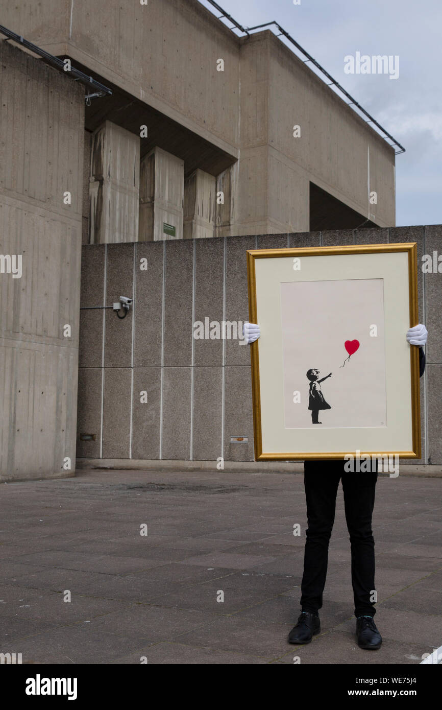 London, UK. 30th Aug, 2019. A Christie's employee poses with artworks 'Girl with balloon' by anonymous street artist Banksy at the Southbank Centre in London Friday, August 30, 2019. The Southbank Centre was near one of the original locations the artwork appeared in London. The screen prints will be on sale during an online only auction titled 'Banksy : I can't believe you morons buy this sh*t' presented by Christie's auction house between 11-24 September 2019. Photograph Credit: Luke MacGregor/Alamy Live News Stock Photo