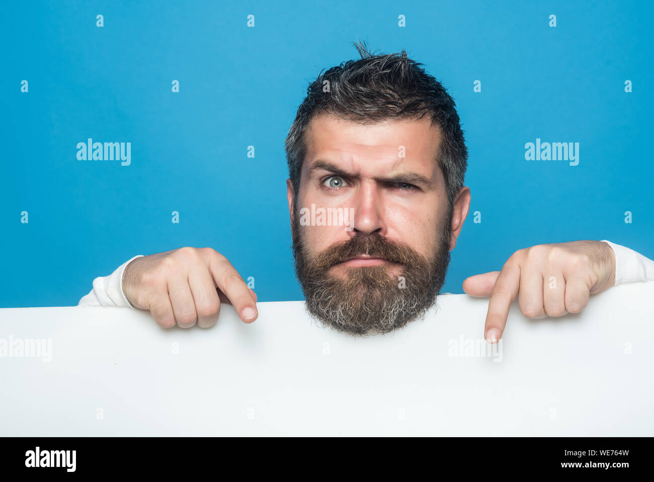Barber fashion and beauty marketing. Guy or bearded man on blue background. Man with long beard and mustache. Hipster with sad face hold paper. Feelin Stock Photo