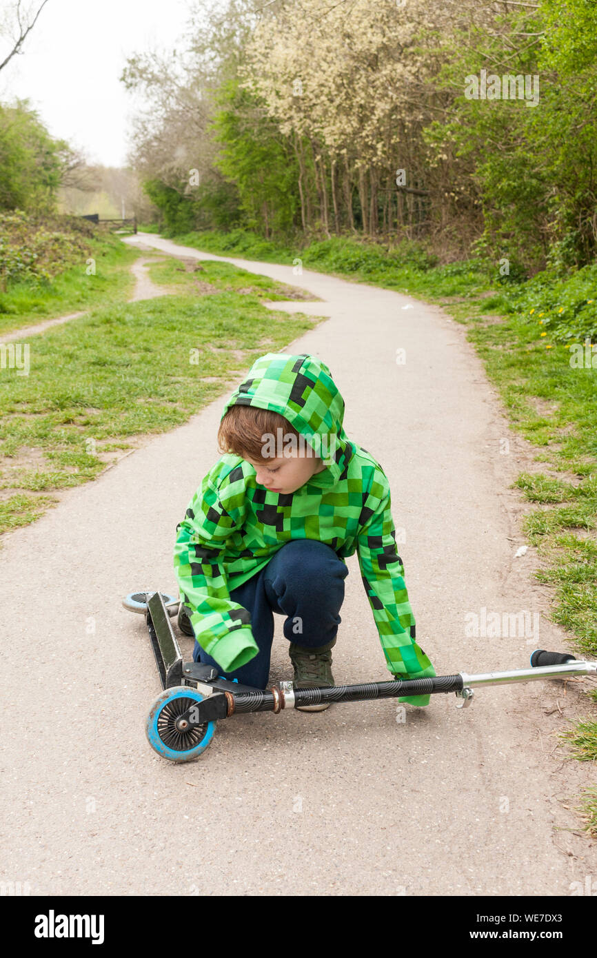 A young boy picking up a scooter outside Stock Photo