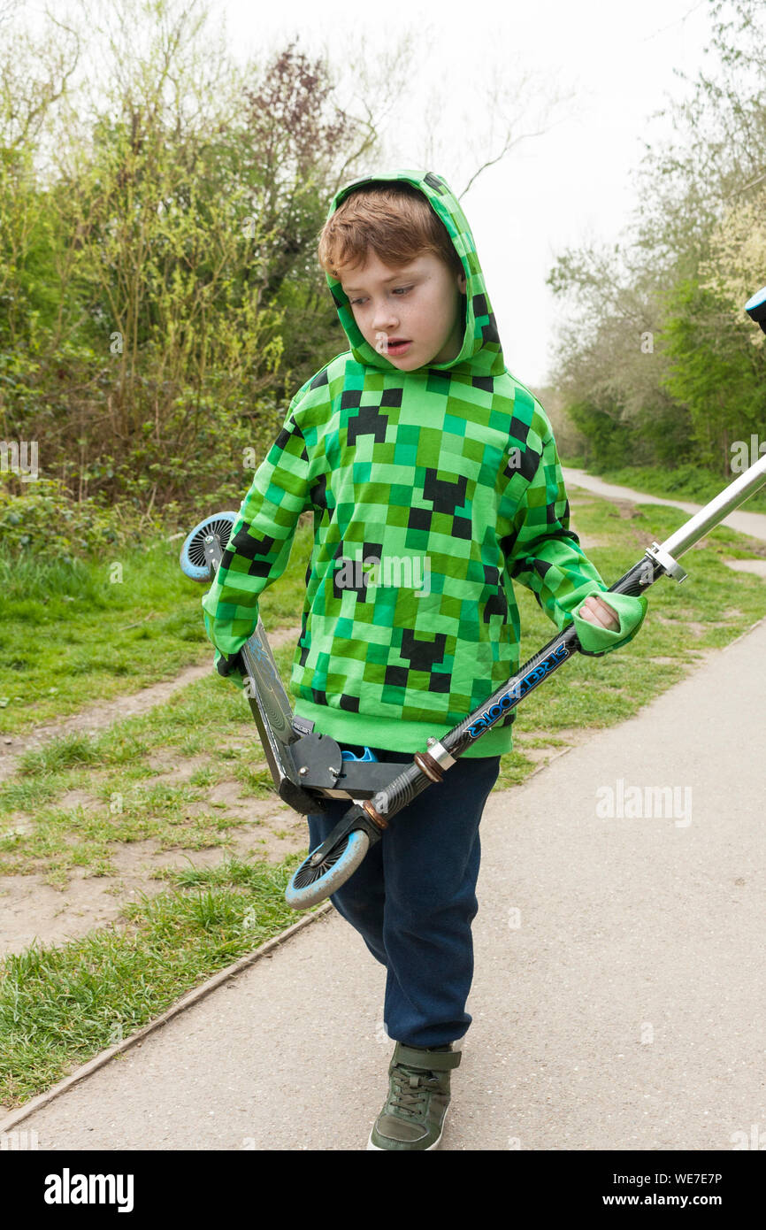 A young boy carrying a scooter in a park Stock Photo