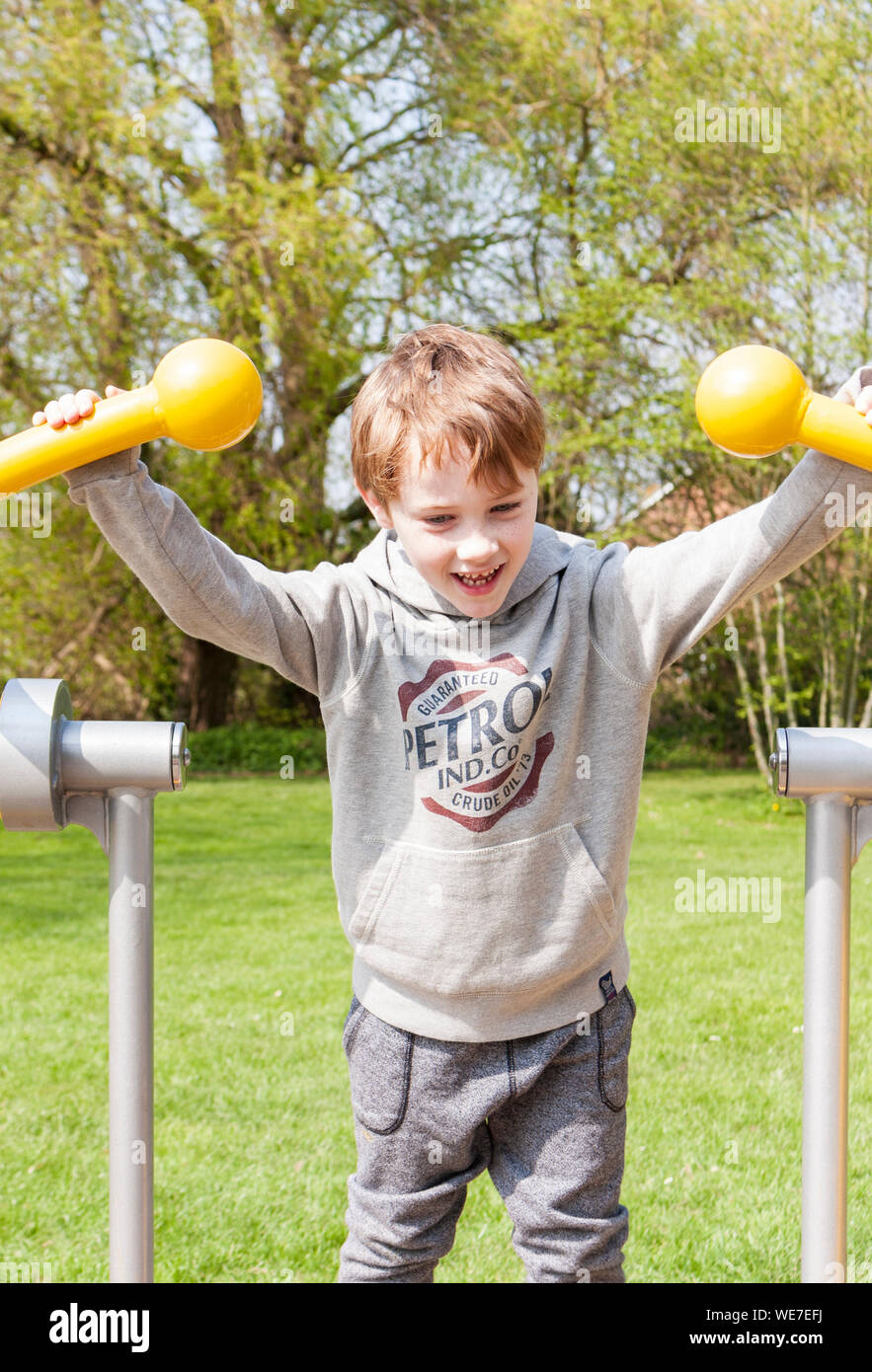 A young boy using the outdoor exercise machine in a park gym Stock Photo