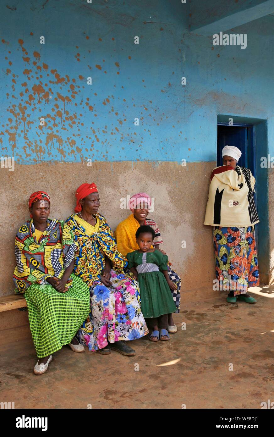 Rwanda, center of the country, villagers in colorful loincloth sitting on a bench in front of a blue wall Stock Photo