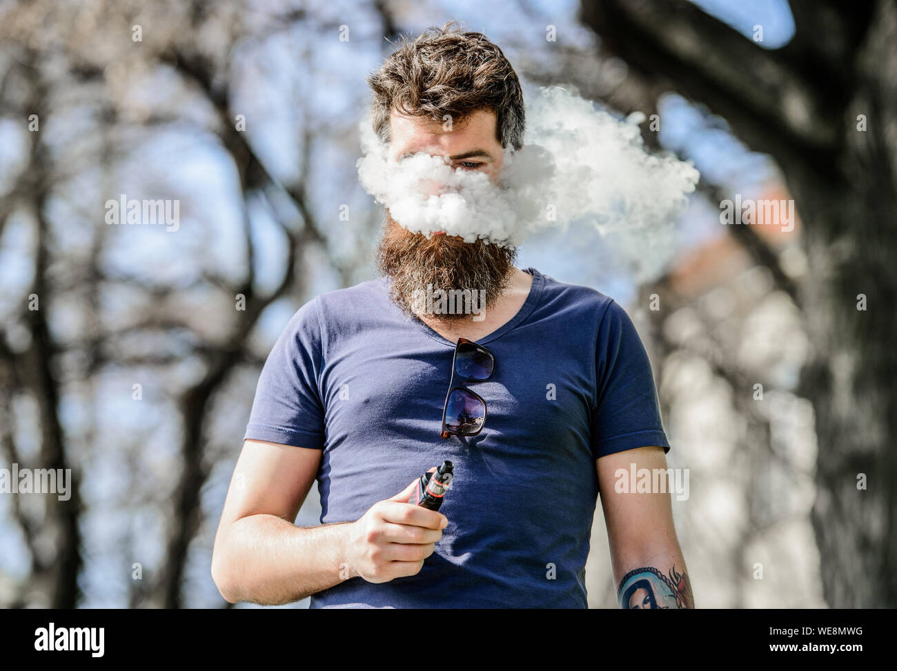 Bearded man smoking vape. Smoking electronic cigarette. Man long beard  relaxed with smoking habit. Man with beard and mustache breathe out smoke.  White clouds of flavored smoke. Stress relief concept Stock Photo -