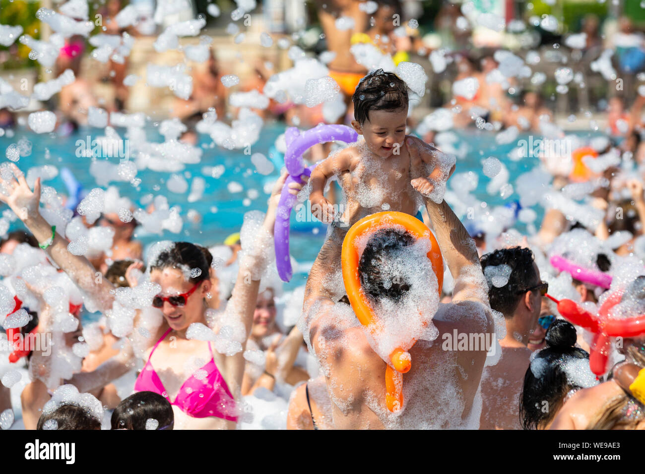 A child is held aloft at a foam party at a swimming pool on holiday