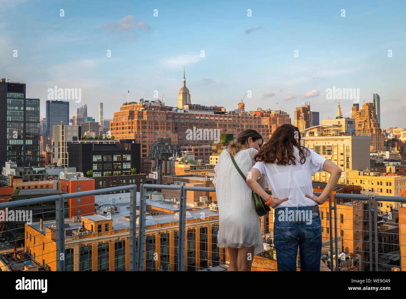 Chelsea New York, rear view in summer of two women friends looking down at buildings in the Chelsea area of downtown Manhattan, New York City, USA Stock Photo