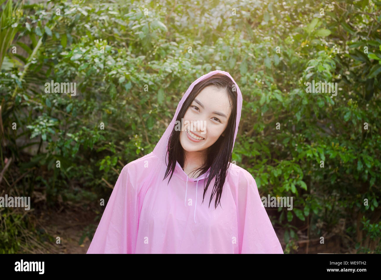 Portrait Of Young Woman In Raincoat Standing Against Trees Stock Photo