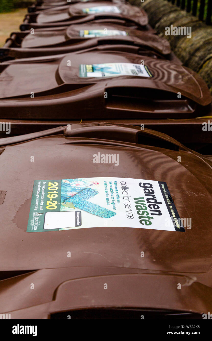 A line of brown garden waste wheelie bins outside a community garden