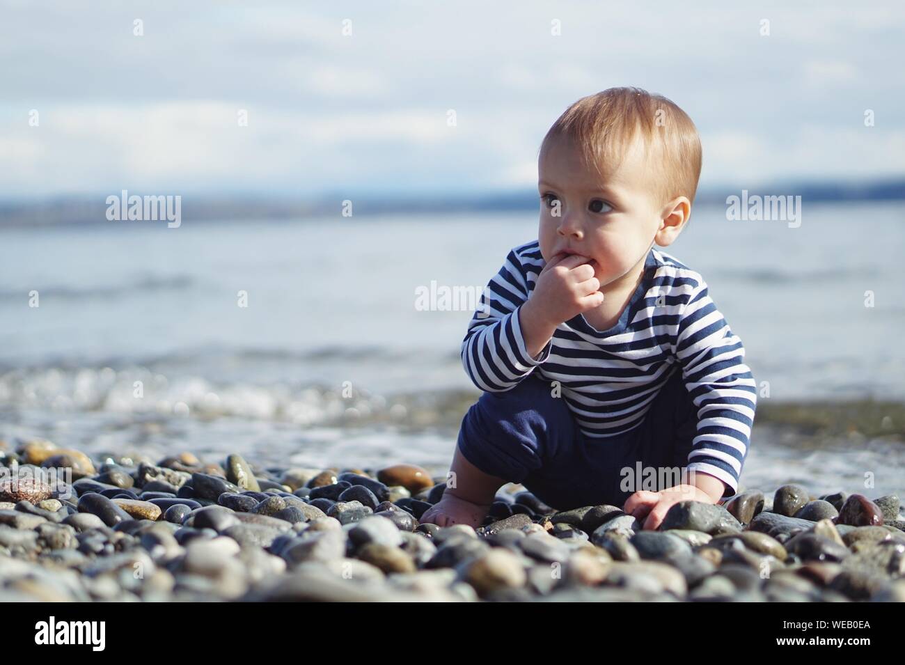 Baby Sitting On Pebbles At Seashore Stock Photo