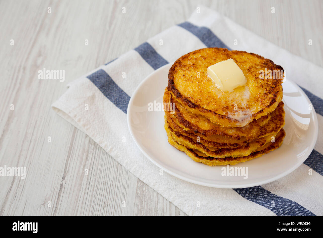 Homemade corn meal Johnny cakes with butter on a white plate, side view