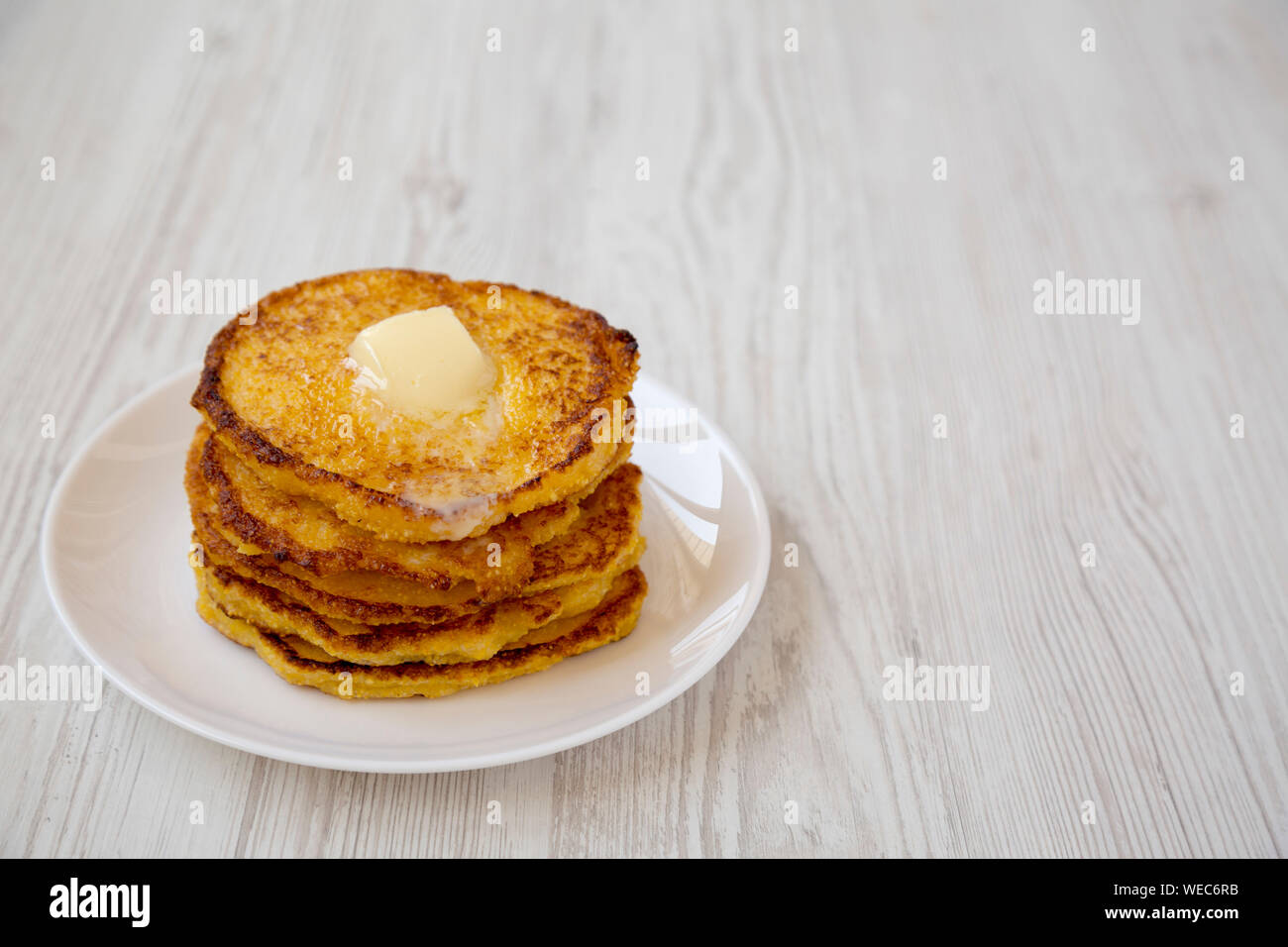 Homemade corn meal Johnny cakes with butter on a white plate over white