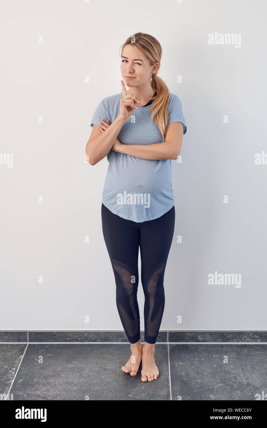 Attractive young barefoot pregnant woman standing thinking or puzzling