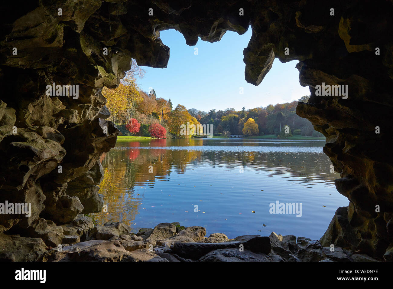 Looking out from the grotto over the lake to distant bridge and colourful trees at Stourhead Wiltshire UK in late autumn Stock Photo
