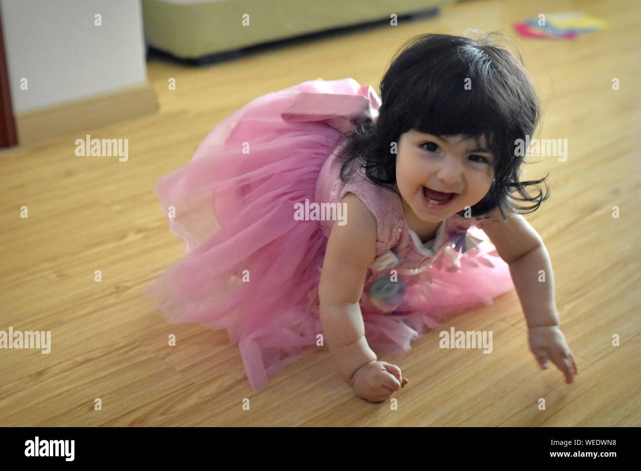 Cute baby girl crawling in pink princess dress and smirking Stock Photo