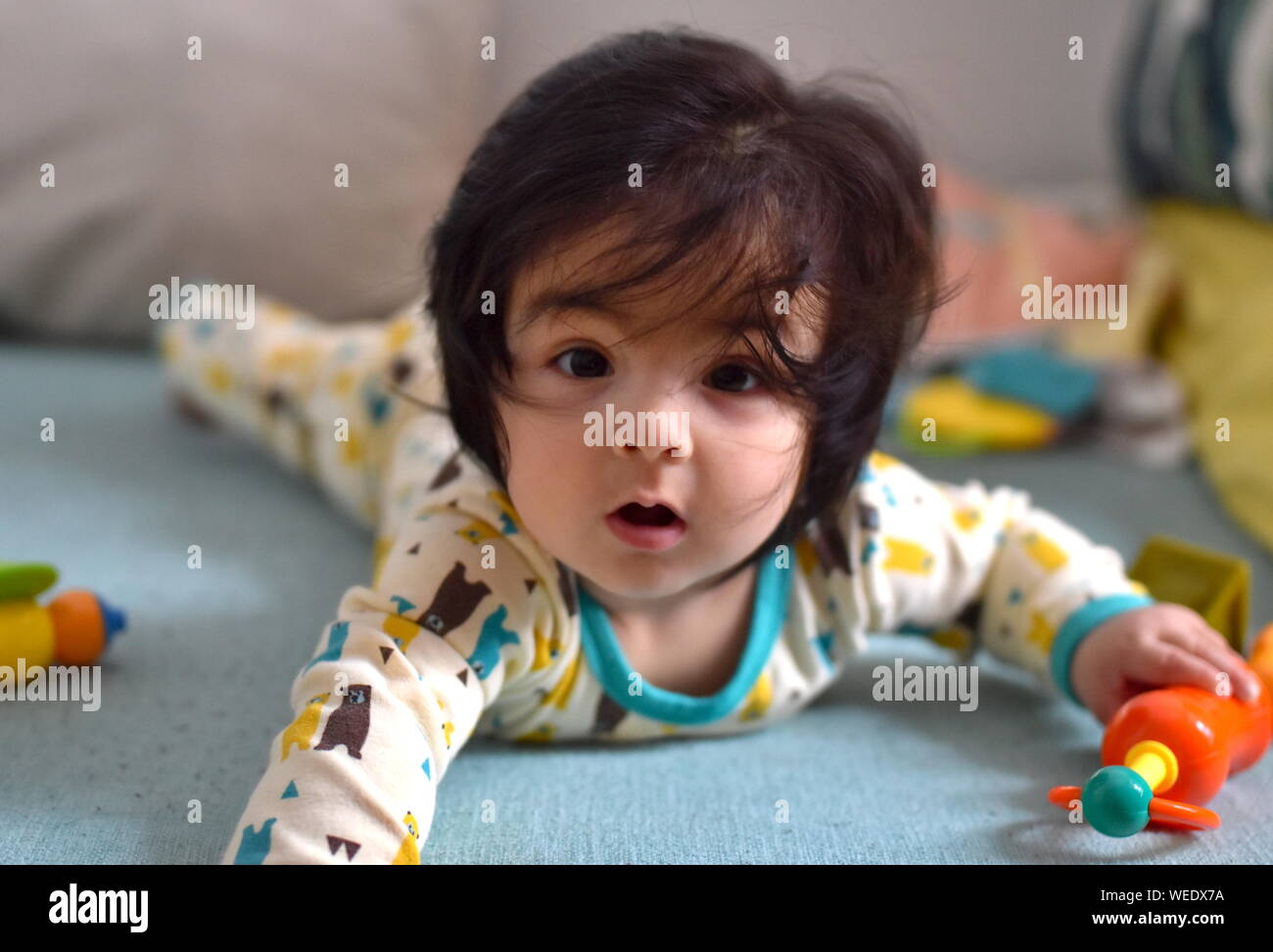 Cute baby mouth open in awe looking at camera surrounded by toys lying down on her tummy Stock Photo