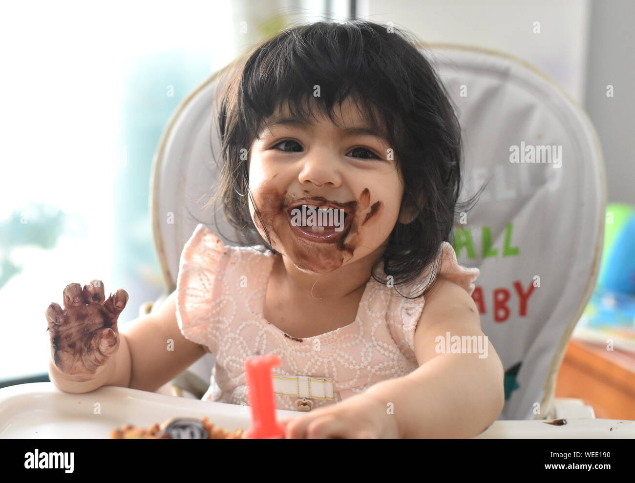 Cute happy baby girl messy eating birthday chocolate cake Stock Photo