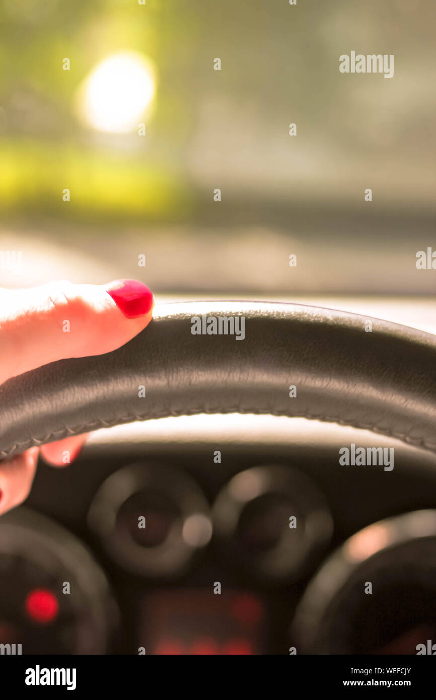 Woman driving a car with one hand holding the steering wheel with natural background rare window view. Selective soft focus. Text copy space. Driving Stock Photo