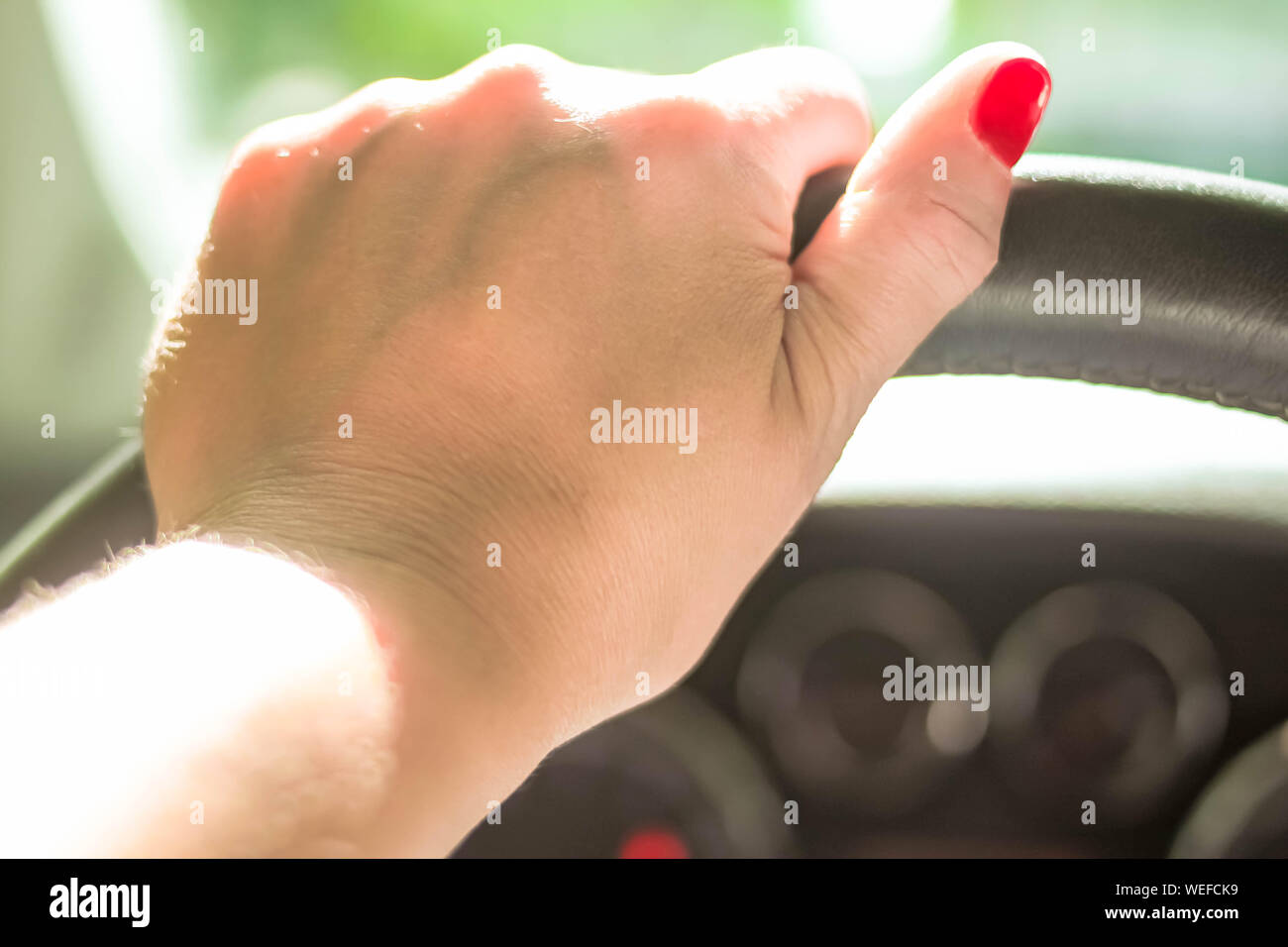 Woman driving a car with one hand holding the steering wheel with natural background rare window view. Selective soft focus. Text copy space. Driving Stock Photo