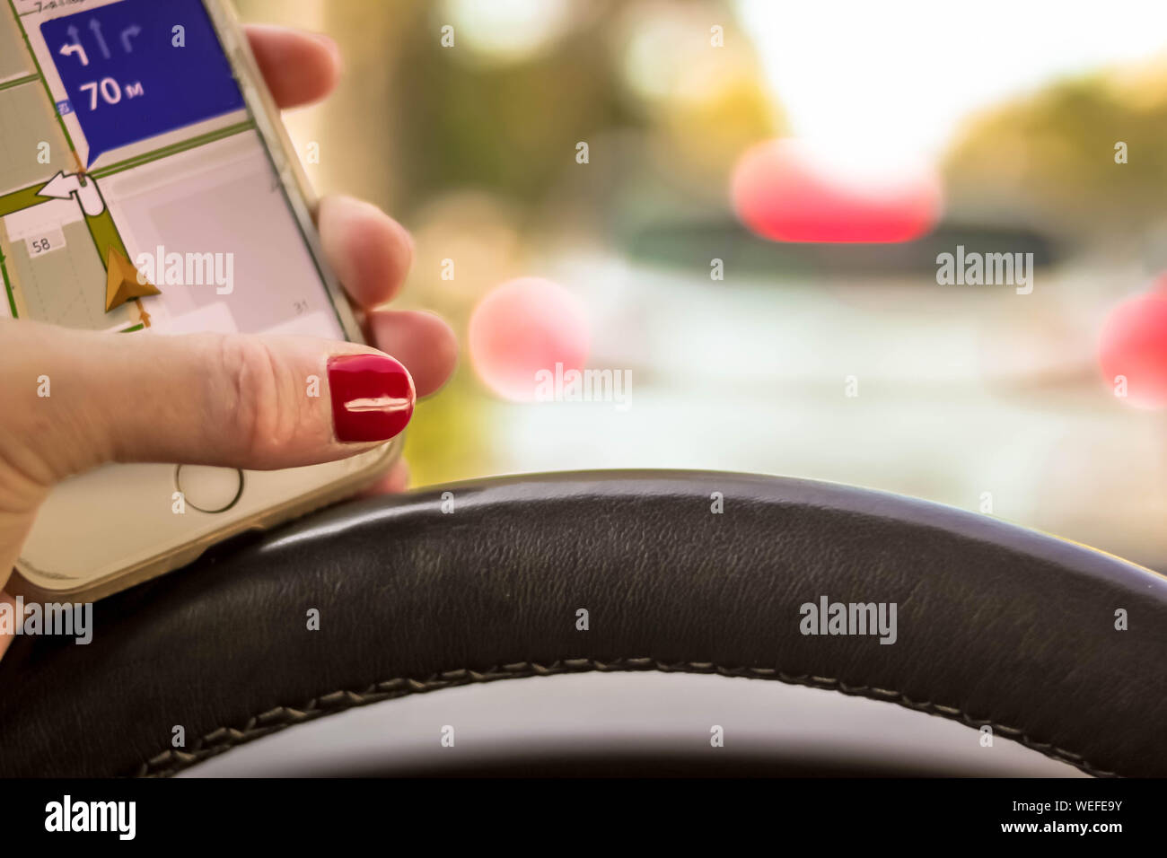 Woman driving a car with one hand holding the steering wheel and mobile phone with navigator map on natural background rare window view. Selective sof Stock Photo