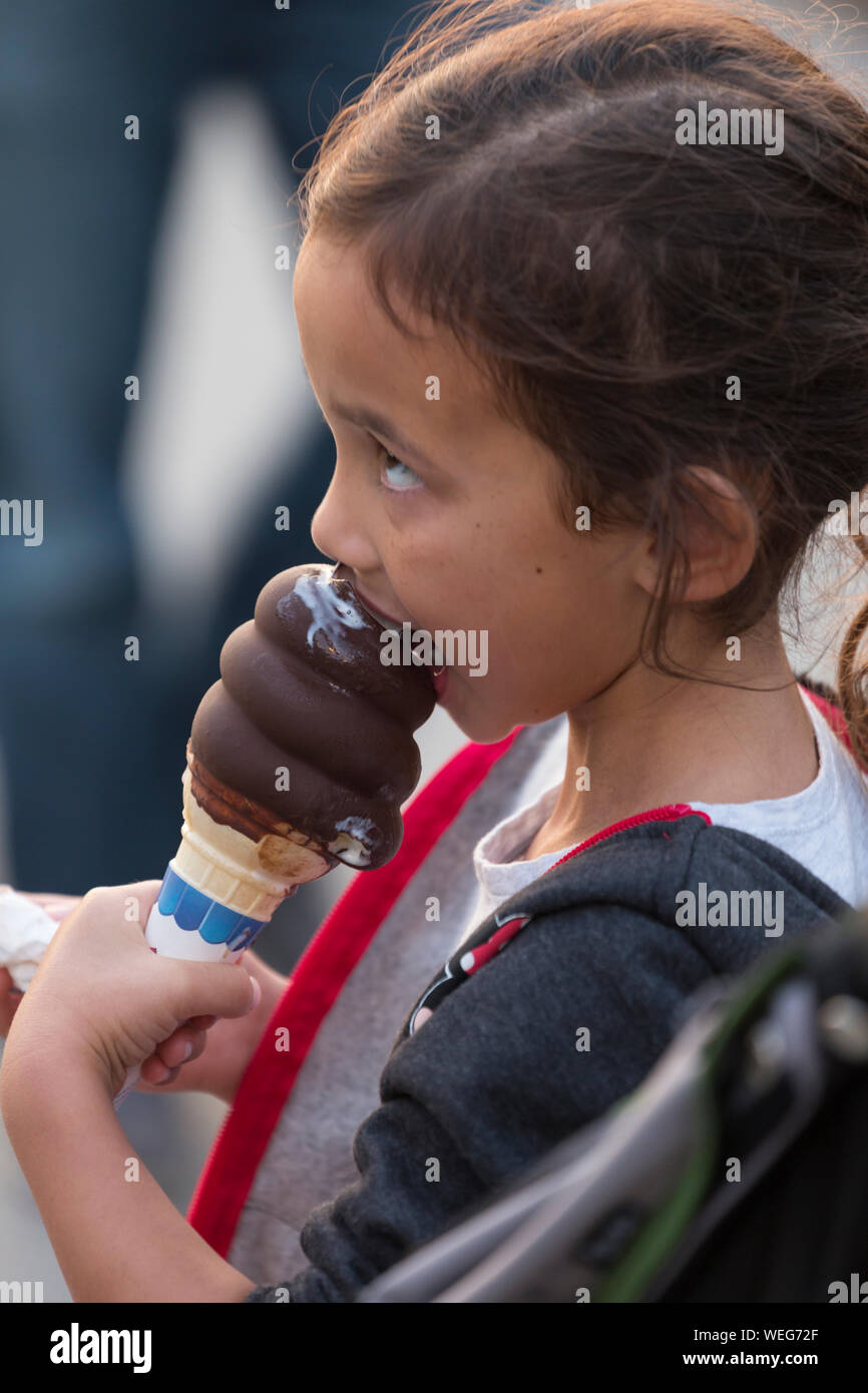 8-9 year old mixed ethnicity Asian girl eating an ice cream cone at a fun-fair in Santa Cruz, California Stock Photo