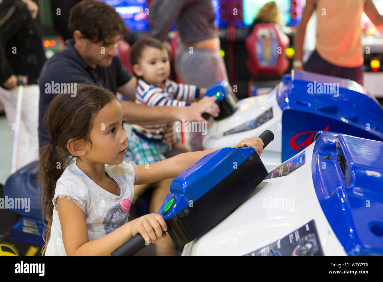 8-9 year old mixed ethnicity Asian girl on game at fairground, father and younger brother in background Stock Photo