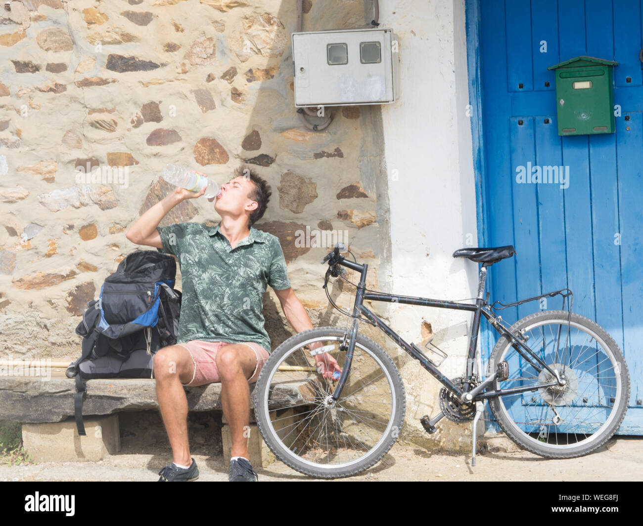 Young Man With Bicycle Drinking Water While Sitting On Seat Stock Photo