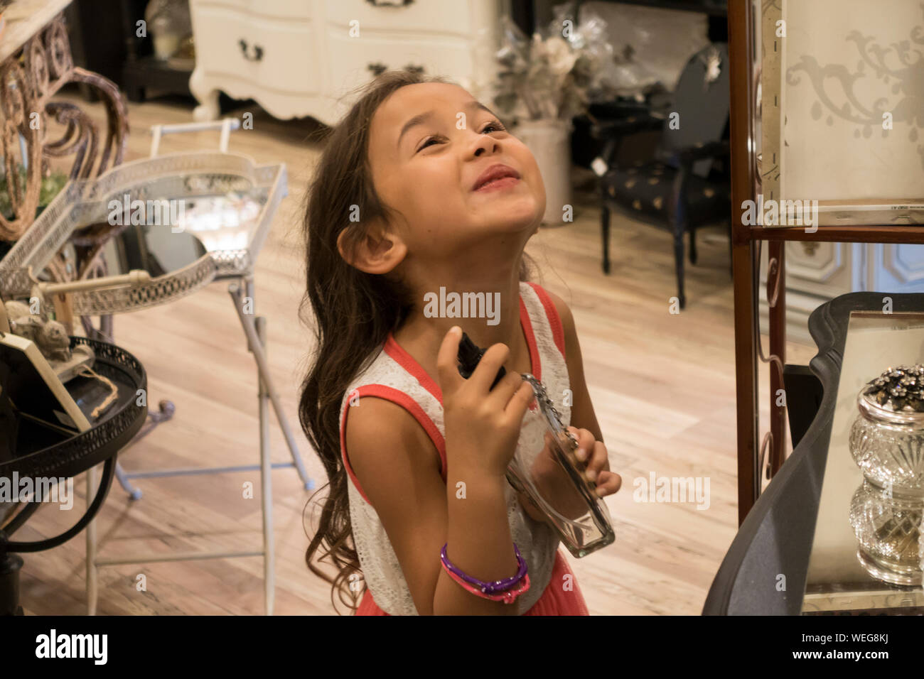 6-7 year old mixed ethnicity Asian girl applying perfume in an antique shop, San Jose, California Stock Photo