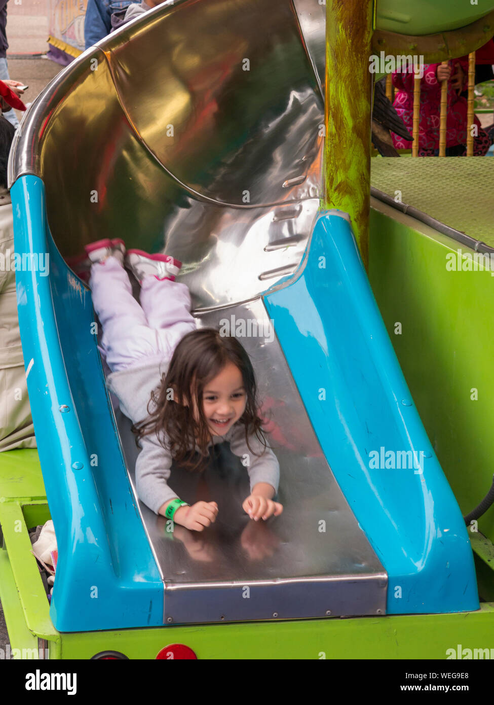 3-5 year old mixed ethnic Asian girl on slide in fairground, laughing, San Jose, California Stock Photo