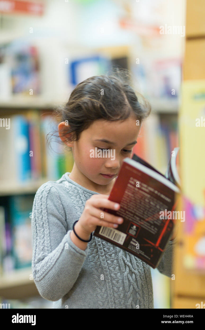 Preteen mixed ethnicity girl looking at books in a bookstore, San Jose, California Stock Photo