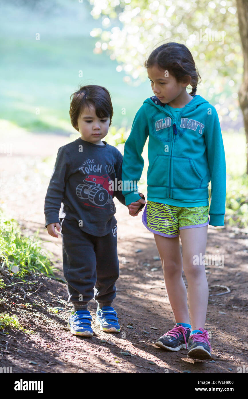 Young sister and brother walking hand in hand on path, San Jose, California Stock Photo