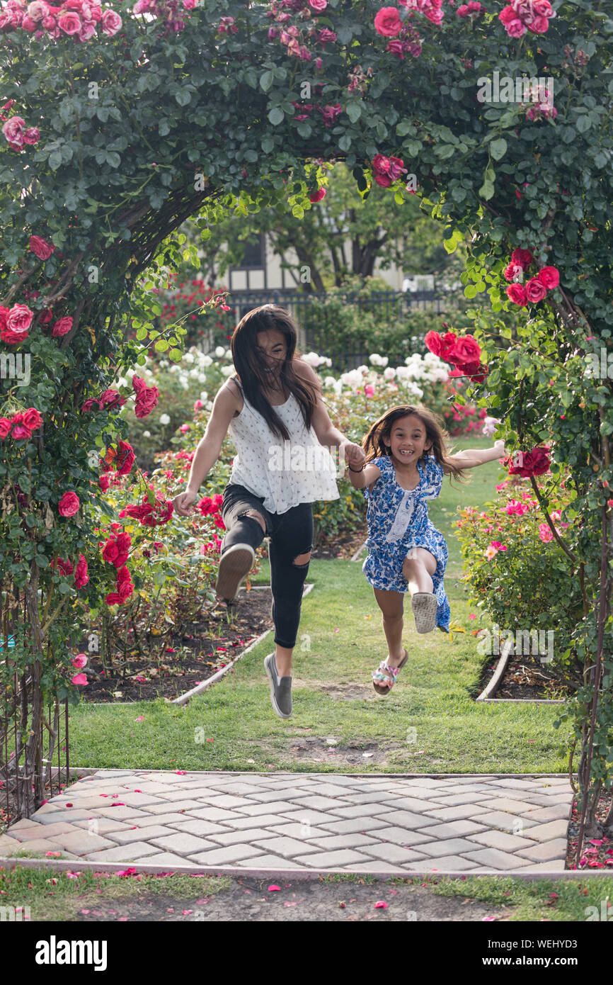 Aisan teenager running, jumping and laughing with preteen sister in rose garden, San Jose, California Stock Photo