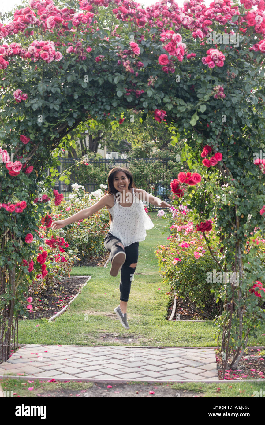 Teenage girl of Asian appearance running and jumping in rose garden, San Jose, California Stock Photo