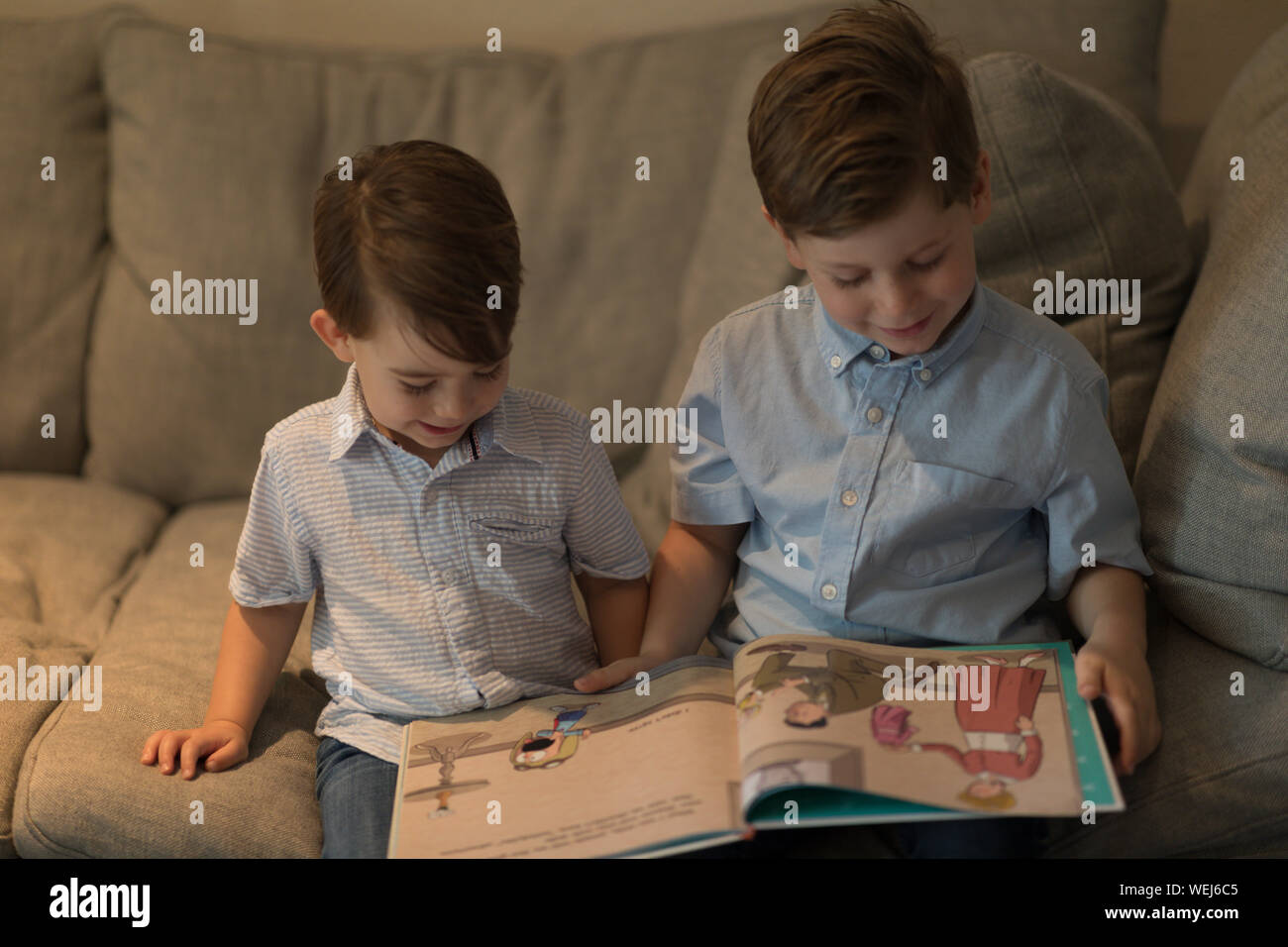 Two brothers, 2 and 4, sitting on sofa looking at book together, Clearwater, Florida Stock Photo