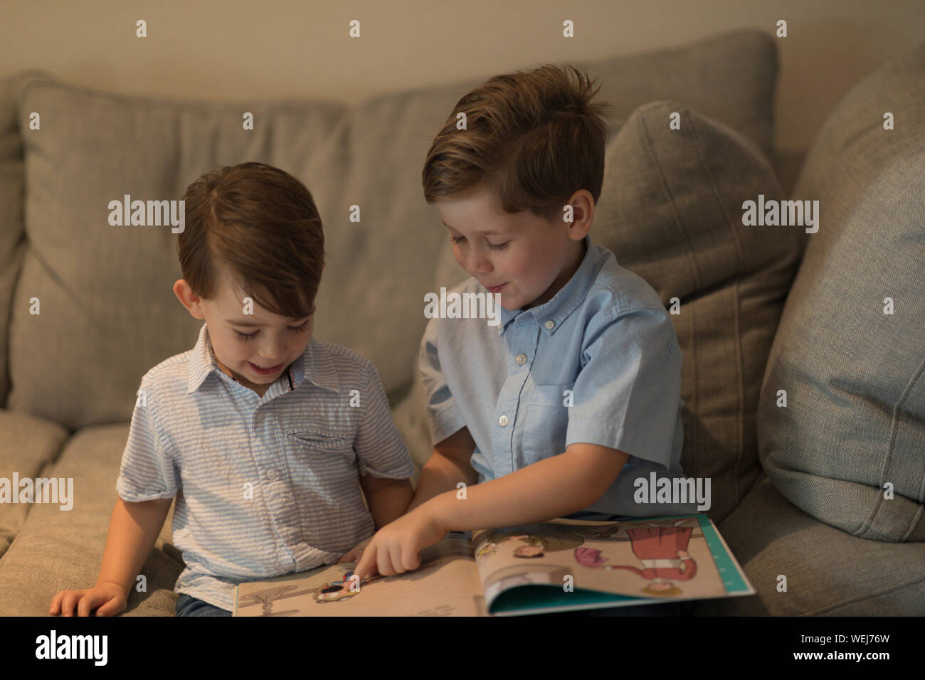 Two brothers, 2 and 4, sitting on sofa looking at book together, Clearwater, Florida Stock Photo