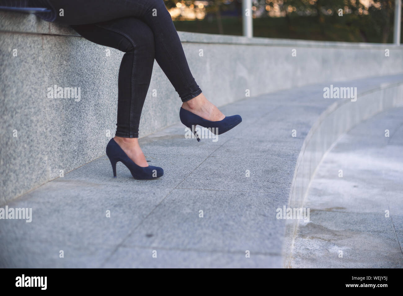 Young office woman blue jeans wearing high-heeled shoes, sitting cross-legged outdoor Stock Photo