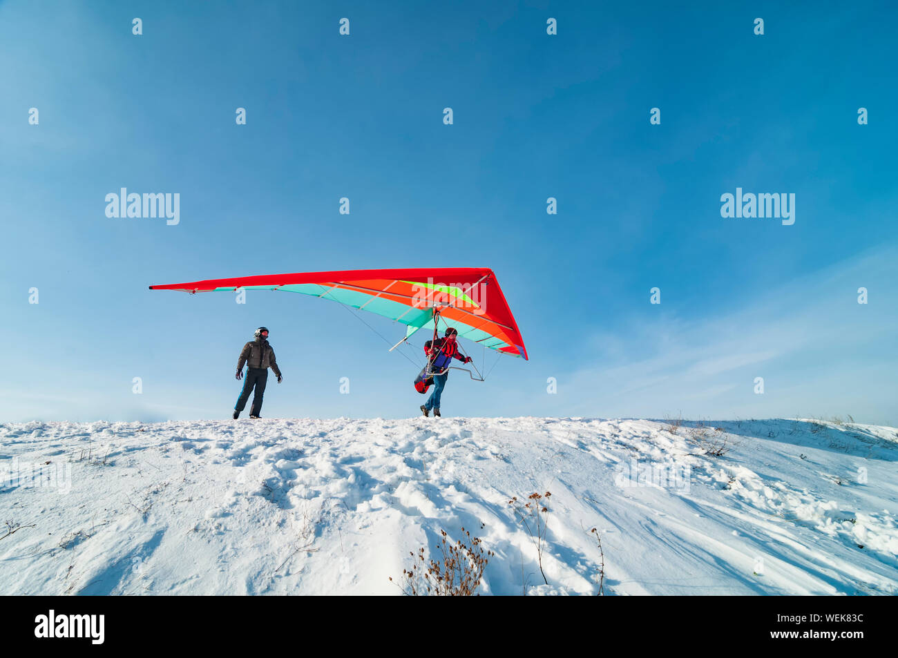Hang glider pilot ready to take off from mountain withhis bright wing. Other pilot is looking at him. Extreme aerial sport. Stock Photo
