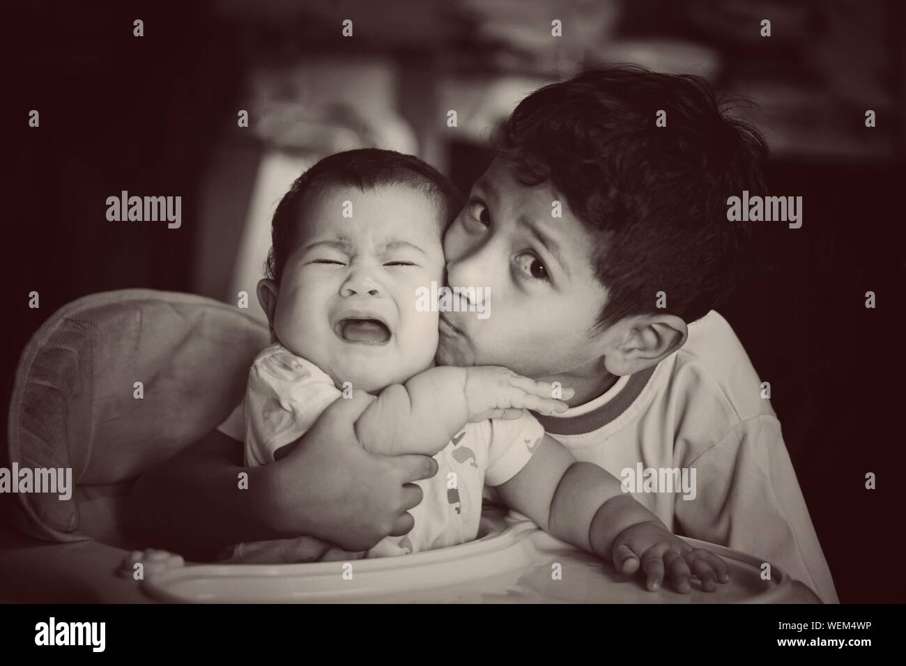 Portrait Of Brother Kissing Sister In Baby Walker At Home Stock Photo
