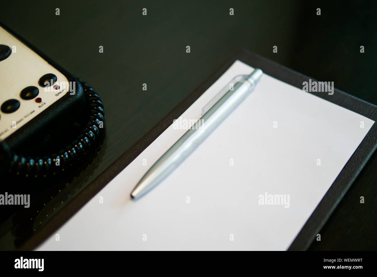 the silver pen color is placed on white short note paper on the brown wooden table near telephone in the luxury hotel room Stock Photo