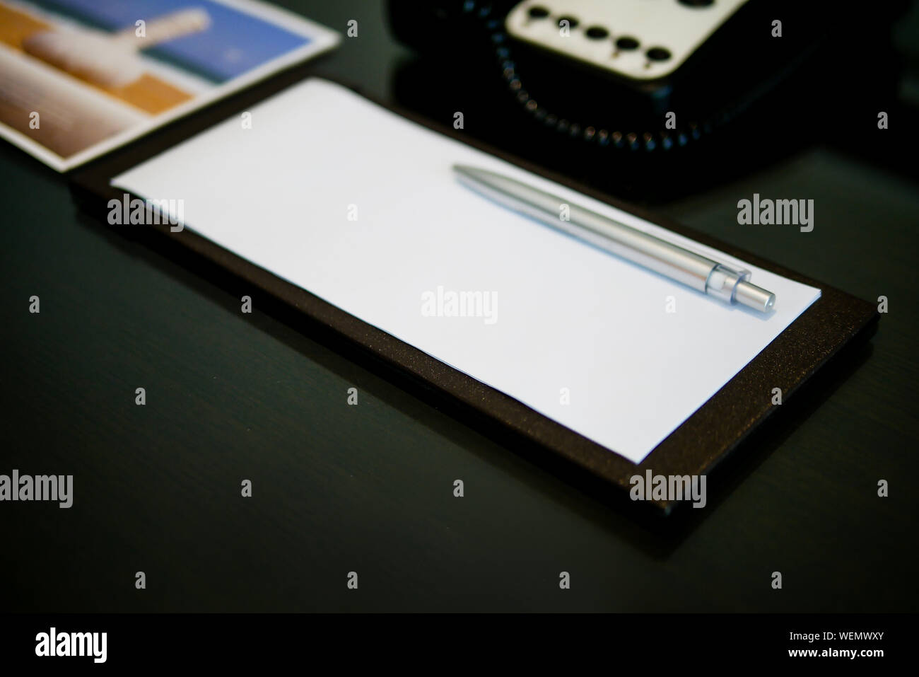 the silver pen color is placed on white short note paper on the brown wooden table near telephone in the luxury hotel room Stock Photo