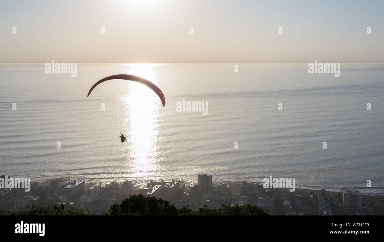 A paraglider launched from Cape Town's Signal Hill at sunset above the  Seapoint suburb on the South African Atlantic shoreline Stock Photo